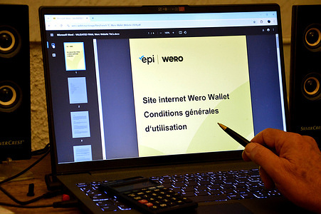 In this illustration photo, a man holding a pen in his hand prepares to read the terms and conditions of use of the European payment application Wero, on his laptop. Created and developed by the European Payment Initiative (EPI), a private company owned by around fifteen European banks, the online payment service Wero (contraction of "We euro") offers a smartphone application for all money transfers and online or in-store payments.