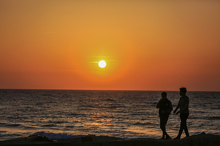 Palestinians walk on the shores of the Mediterranean Sea during sunset in Gaza City.