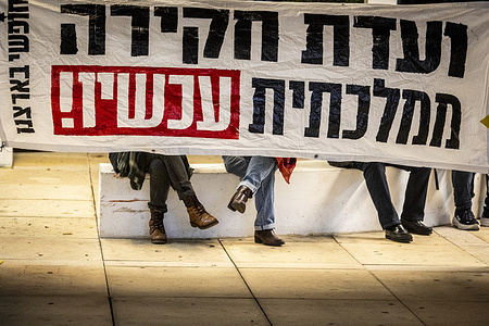 Israelis sit under a banner that reads "A state Commission Inquiry NOW" during a rally demanding a state commissions of inquiry. More than two years after the deadliest day in Israel's history, the government has still not established a formal state commission of inquiry into the security and intelligence failures that allowed Hamas to kill more than 1,200 Israelis and kidnap over 250 others. Instead, ministers advanced an independent commission on Sunday, promising broad public representation and full investigative powers, while tasking a ministerial committee, appointed by Netanyahu, to define its mandate within 45 days. Bereaved families and survivors, organized as the October Council, condemned the move as a political manoeuvre and vowed to escalate their protests.