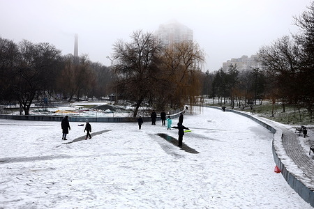 People walk on the frozen water of an artificial reservoir at Victory Park. Despite Russia's ongoing military aggression and power outages, city residents are trying to live their normal lives.