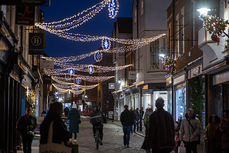 Shoppers walk under the Christmas lights at the city centre in Canterbury. Canterbury Christmas Market is considered the largest in whole Kent, England. It features around 120 wooden huts hosting over 170 stallholders. It is from two parts one is located by the Canterbury Cathedral and the other one on the High Street at the city centre.
