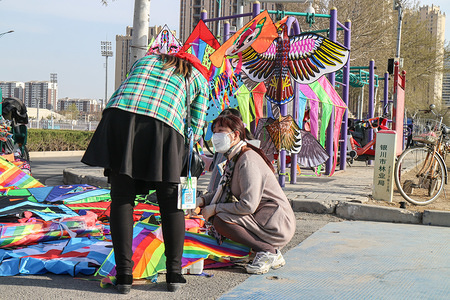 A woman wearing a protective mask sales kite at a public square in Yinchuan.