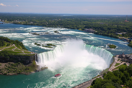 Aerial view of Horseshoe Falls of the Niagara Falls is seen on a hot and sunny day. Niagara Falls is the collective name for three waterfalls - a Horseshoe Fall, an American Falls and a Bridal Veil Falls which is straddle the international border between Canada and the United States; more specifically, between the province of Ontario and the state of New York.