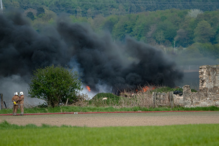 2 firemen looking on-wards towards the blaze. Fire fighters have been called out to deal with a fire in Airth, Falkirk. 3 trucks and 5-8 fighters present on scene. Police have the road up to it locked off.