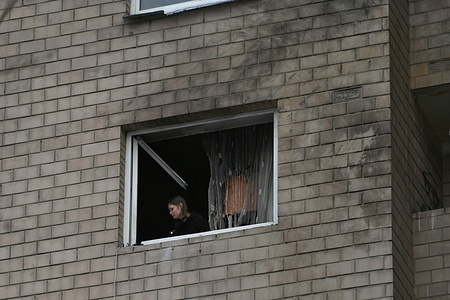 A woman cleans a balcony from shrapnel in a damaged house after a drone strike in the Shevchenkivskyi district of Kyiv. The aftermath of the drone strike on a building shows a playground in front with people clearing debris on Oleny Telihy Street in Kyiv, Ukraine on December 28, 2025. The structure was damaged by a Russian Shahed drone attack, and emergency services along with residents are working to secure the area and assist those affected.