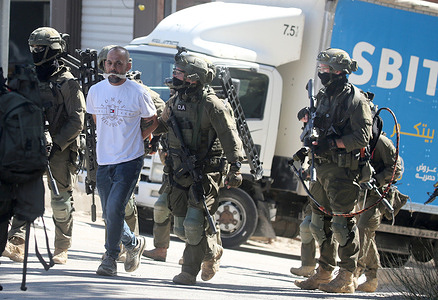 Israeli soldiers lead a handcuffed and gagged Palestinian detainee during a raid on the Askar refugee. Israeli forces raided and searched Palestinian homes and shops damaging their contents. They also launched an arrest campaign targeting dozens of Palestinian civilians.