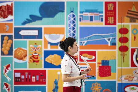 A Cathay Pacific airline worker is seen in front of a Hong Kong–themed illustration collage at Chek Lap Kok International Airport.