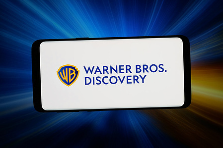 In this photo illustration, the logo of the US company Warner Bros. Discovery, Inc. (WBD) is displayed on a smartphone in front of an abstract background on a computer screen.