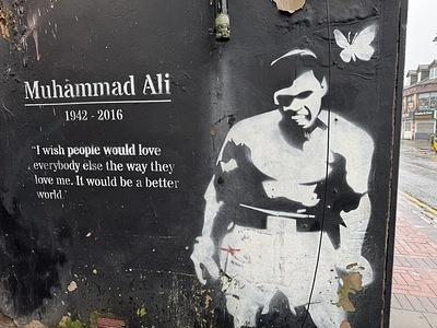A black-and-white stencil mural of Muhammad Ali is seen on a wall in Birmingham, featuring the quote: “I wish people would love everybody else the way they love me. It would be a better world.”