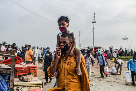 A migrant man wearing a facemask carries his child on his shoulders as he walks to the ferry during eid al-fitr.Migrant people get onto an overcrowded ferry to travel home for Eid al-Fitr festival amid concerns of coronavirus (COVID-19) outbreak in Munshiganj district.
