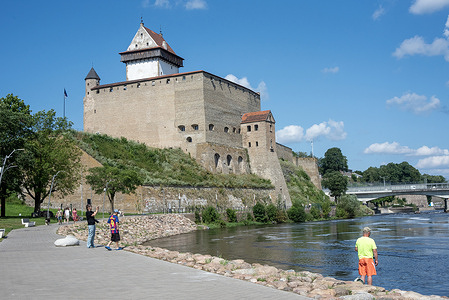 People enjoy the beautiful weather on the riverbank of the Narva River in Narva City. Narva is a city located on the easternmost edge of Estonia, bordering Russia. It offers a unique blend of historical influences, shaped by its strategic location and complex past. The city features a mix of medieval fortifications, Soviet-era architecture, and contemporary Estonian culture, all set along the scenic Narva River.