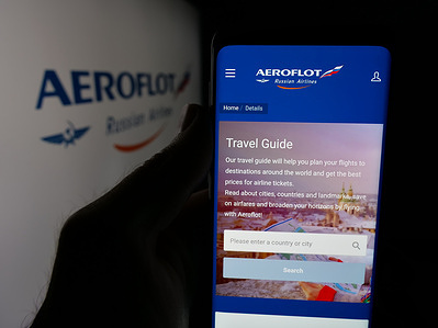 In this photo illustration, a person is holding a smartphone with the web page of company PJSC Aeroflot - Russian Airlines on screen in front of logo.