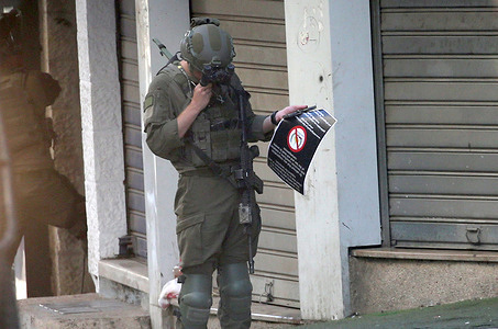 An Israeli soldier holds a sign announcing the closure of the Palestinian Solidarity Association compound in downtown during a military operation. During a military raid in the West Bank city of Nablus, the Israeli army forcibly shut down the headquarters of the Attadamun Charitable Society, a prominent local organization that provides vital care and aid to thousands of Palestinian orphans and widows. Troops confiscated the charity’s equipment and welded the building's doors shut, leaving behind an official military order that closed the complex under allegations of supporting terrorism.