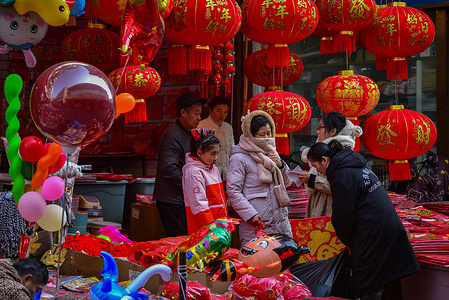 A group of customers shop for red Spring Festival decorations at a lively stall adorned with colorful balloons at Sanliwan Commodity Market.