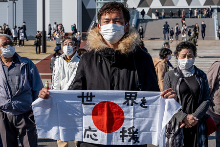 A man holding a Japan national flag with 'supporting the world' written on it. 'Flame of Recovery' special exhibition at Aquamarine Park after it was announced that the Tokyo Olympic and Paralympic Games 2020 are to be postponed due to coronavirus (COVID-19) pandemic.