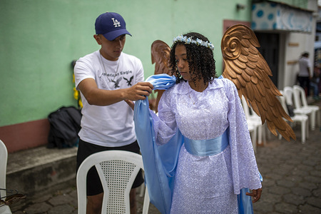 A man helps his daughter dress as an angel during the celebration of the Dance of the 24 Devils in Ciudad Vieja, Sacatepequez, as part of the Day of the Immaculate Conception. The Dance of the 24 Devils is recognized as an Intangible Cultural Heritage of Guatemala. In this traditional performance, the devils represent evil, while figures like Death and the Archangel Saint Michael take part in a symbolic battle between good and evil.