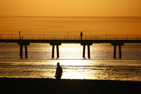 A man walks along Altona Pier during sunrise at Altona Beach. The weather is expected to reach a maximum of 36 °C with inland areas exceeding 40 °C. The Bureau of Meteorology has issued a severe heatwave warning for Victoria. Residents are advised to remain hydrated, limit prolonged sun exposure, check on vulnerable individuals, and follow official heat health guidance.