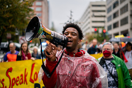 A man chants slogans on a megaphone before marching to the IMF Building. Demonstrators gathered in Edward R. Murrow Park and made noise with drums, horns, whistles, and other items as they raise their voices about the governments of the world making money of fossil fuels without trying to fund a transition to clean energy. Later they marched towards the building where the G20 IMF Press Conference was being held, amassing on the sidewalk.