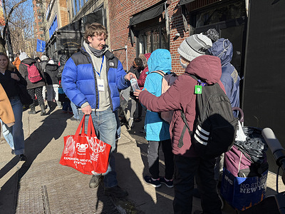 An employee of Polymarket hands out free bottles of water to people waiting in line in front of the store. The establishment officially opened at 2pm today, for what is called 'New York's First Free Grocery store' in the West Village.  Tickets were given out hours before and many shoppers started waiting in line at 7am. They were given a bag and could fill the bag with free groceries to the brim .