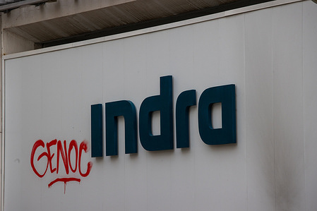 Graffiti is painted on the Indra headquarters logo in Madrid, creating a Spanish pun: "Genoc-Indra," likening it to "Genocida" (Genocide). Activists from the Extinction Rebellion group protested in front of Indra's headquarters in Madrid, as part of the COP30 summit in Brazil, to denounce the militaristic drift and demand that the Spanish government allocate resources to climate and social policies instead of the military industry.