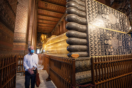 A foreign tourist wearing a face mask admires the large gilded statue of the Reclining Buddha in Wat Pho. Wat Pho (also spelled Wat Po) is a Buddhist temple in the Phra Nakhon District of Bangkok. Foreign tourists slowly coming back to Thailand during the "Test & Go" program, including the 1 day quarantine entry scheme for fully-vaccinated international tourists. The World Health Organization (WHO) has recorded a total of 3,303,169 infections and 24,075 deaths in Thailand since the beginning of the Covid-19 outbreak.