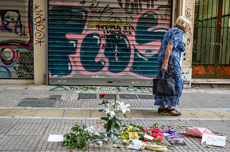 An old woman seen walking next to the flowers and candles left for Zak Kostopoulos (33 years old) who was killed last Friday after attempting to rob a jewellery store in Athens, police said.