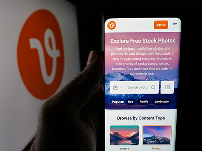 In this photo illustration, a person is holding a smartphone with the webpage of stock marketplace company Eezy LLC (Vecteezy) on screen in front of logo.