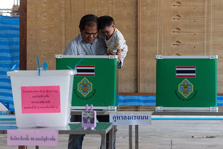 A man with a kid casts his ballot at a polling station during Thailand's general election in Bangkok.