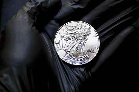 In this photo illustration, a person wearing black latex glove holds a 1 USD silver coin in his hand.