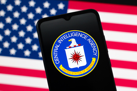 In this photo illustration, the CIA (Central Intelligence Agency) logo is seen displayed on a smartphone screen and the United States flag in the background.