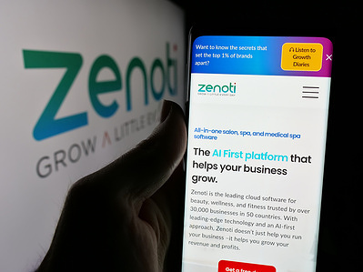 In this photo illustration, a person is holding a mobile phone with the website of US salon software company Soham Inc. (Zenoti) on screen with logo.