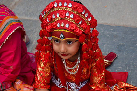 A young girl under the age of 7 adorned as a Goddess participates in the mass Kumari Puja rituals in Kathmandu Durbar Square. Hundreds of young girls gathered to offer worship for good luck, protection from the evil spirits and to prevent diseases. Kumari Puja is celebrated through a ceremonious worship of young girls as manifestations of the divine female energy or Goddess.