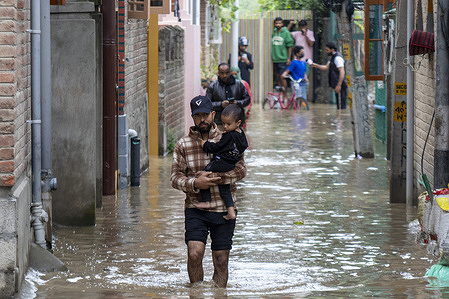 A man carries his child as he wades through a flooded street in the capital city Srinagar. Torrential rains swelled Kashmir’s Jhelum River past the danger mark on Wednesday, prompting officials to declare a flood, as landslides and fierce floods unleashed in the neighboring Jammu region killed more than 30 people, swept away homes, roads and bridges, and cut off telecommunications across large parts of the Himalayan territory.