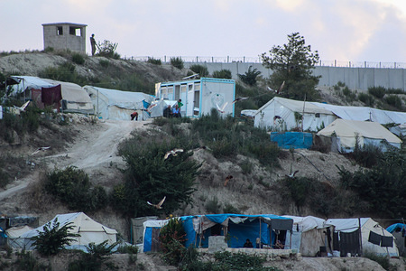 A soldier is seen standing next to the separation wall between Syria and Turkey and is surrounded by camps for the displaced from the areas of Latakia and its countryside.