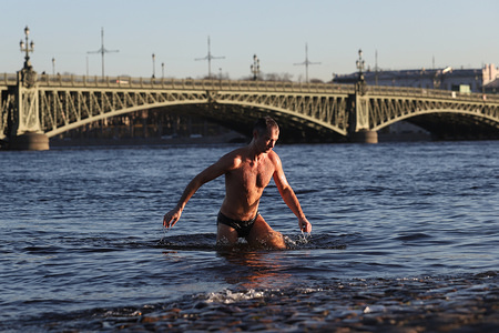 A man gets out of the Neva river during sunny day. 
Temperature dropped to minus 2º degrees.