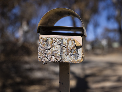 A letterbox showing significant fire damage. One month after bushfires damaged sections of the township and surrounding farmlands, destroyed properties and infrastructure remain visible and community recovery efforts are steadily progressing. 
Local volunteers and residents continue rebuilding, reflecting the town’s resilience in the aftermath of the disaster.