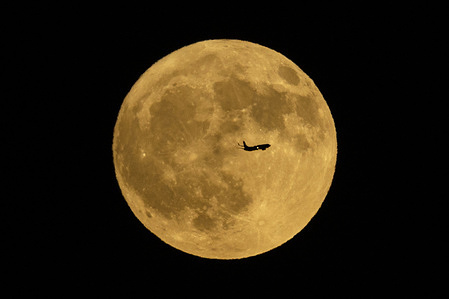 An airplane flies past an almost full moon rising over Los Angeles.