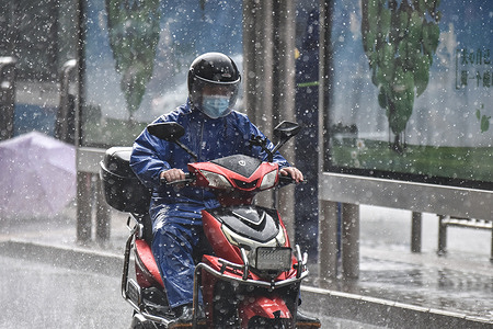 A man wearing a raincoat seen riding an electric bike during the rainstorm.Beijing took multiple measures on Monday to cope with the heaviest rain to hit the capital this year. Kindergartens, primary and secondary schools in the city suspended classes on Monday and company employees were encouraged to work from home or alter their travel times.