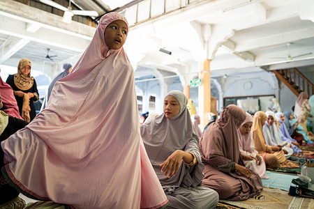 A young girl is helped to adjust her prayer garment among women gathered for Eid al-Fitr prayers at a mosque as Ramadan comes to an end. Muslim women attend morning prayers at a mosque in Narathiwat on March 21, 2026, as Thailand marks Eid al-Fitr, the end of Ramadan.