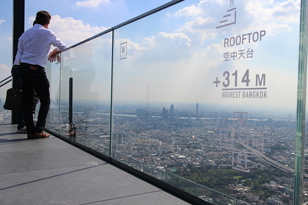 Two men seen leaning against a glass barrier on the higher rooftop of Bangkok.
In November 2018, Mahanakhon Tower opened a rooftop featuring a glass sky walk of 314 meters height. It is today the highest observation point of Bangkok.