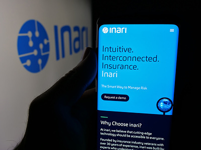 In this photo illustration, a person is holding a cellphone with the webpage of Spanish company Inari Enso SL (inari.io) on screen in front of logo.