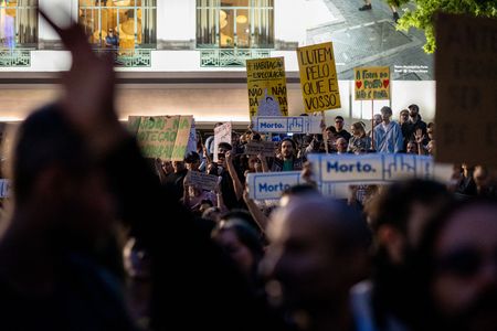 People holding placards gather at Praça D. João I during a demonstration in support of housing rights and against police violence in the city. Activists and supporters gathered in the square following clashes between police and participants of a housing protest camp. The public assembly was held one day after clashes between activists and police.