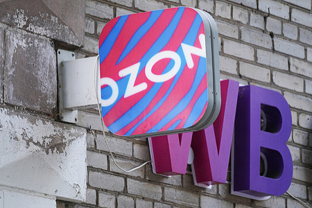 A close-up view shows the corporate signboards of Russia's leading e-commerce marketplaces, Ozon and Wildberries (WB), installed on a wall of a building. In Russia, entrepreneurs frequently open multi-branded pickup points (PvZ) representing several major digital platforms in a single location to optimize operational costs and attract a larger volume of customer traffic.