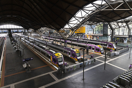 V-Line trains are seen idle at Southern Cross Station, as only a few rural train lines remain open. As Melbourne endures searing 40°C heat and strong winds, bushfires continue to burn across the state. In the city, residents grapple with the extreme conditions, while public transport is disrupted and rural train services are suspended.
