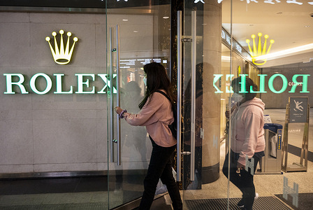 Shoppers walk past the Swiss luxury watchmaker Rolex logo and store in Hong Kong.