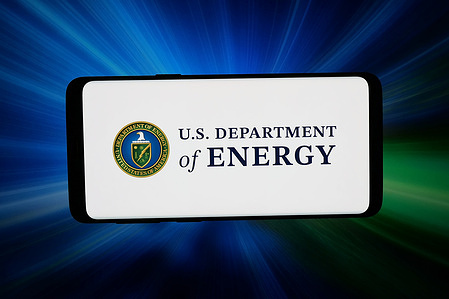 In this photo illustration, the United States Department of Energy (DOE) logo is seen displayed on a smartphone in front of abstract background on computer screen.