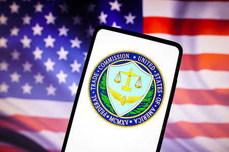 In this photo illustration, the United States Federal Trade Commission (FTC) logo is displayed on a smartphone screen with a United States flag in the background.