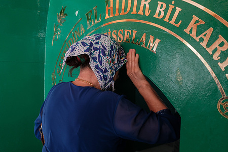 A woman kisses the door as she enters the shrine during the event. The Feast of Ghadir al-Hum was celebrated by burning bahur and prayers at the tombs in Harbiye in Hatay's Defne district. This holiday is commemorated by Arab Alawites and Shia Muslims as the day when Prophet Muhammad honored Prophet Ali on his return from the Farewell Pilgrimage. In Turkey, this holiday is mostly celebrated in provinces such as Hatay, Adana and Mersin, where Arab Alevis live in large numbers. One of the most important events of this holiday is the preparation and distribution of hrisi, a dish made by beating wheat and meat together in large cauldrons.