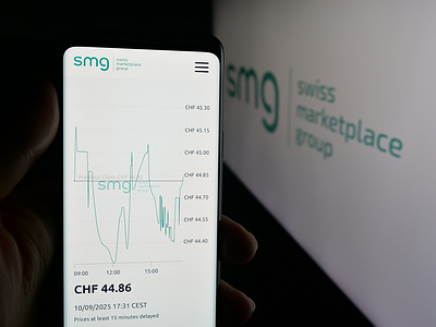 In this photo illustration, a person is holding a cellphone with the webpage of company SMG Swiss Marketplace Group AG on screen in front of logo.