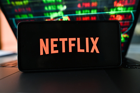 In this photo illustration, the Netflix logo is displayed on a smartphone with stock market percentages in the background.